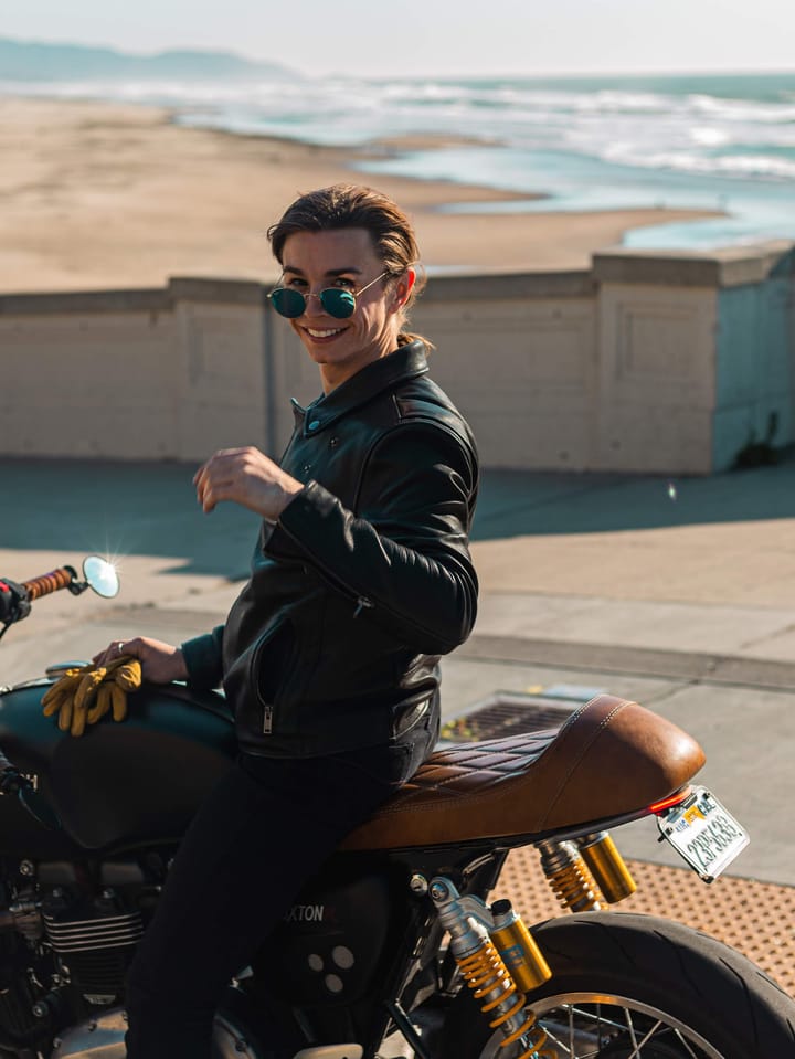 Grace sitting on her Triumph motorcycle beside the sea.