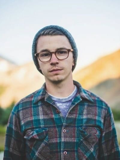 An earlier outdoor portrait of Grace in a beanie, glasses and plaid shirt.